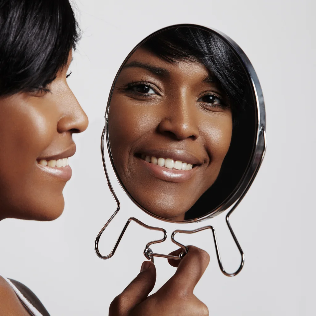 Woman smiling at her reflection after aesthetic skin treatment at Two Chicks Aesthetics in Port Jefferson NY