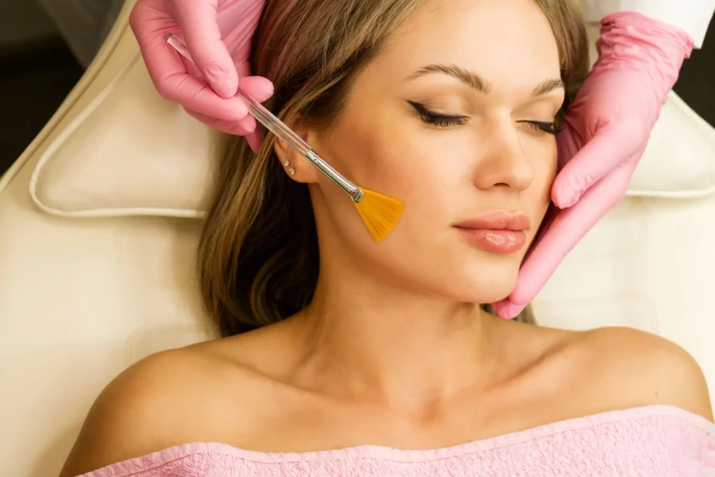 Aesthetician applying chemical peel solution to a client’s cheek with a fan brush