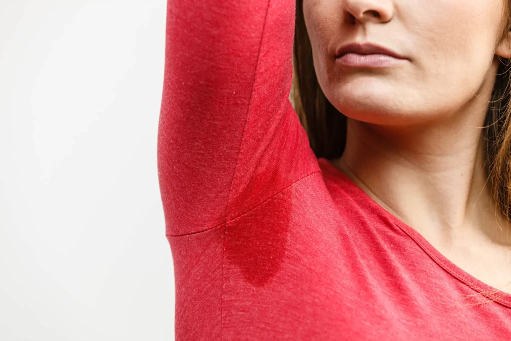 Person lifting arm showing underarm sweat stain on a red shirt
